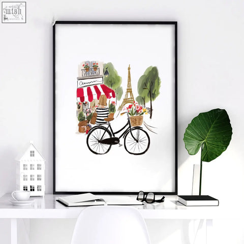 Black-framed paris wall art featuring a woman on a bicycle with eiffel tower and café in a floral basket design
