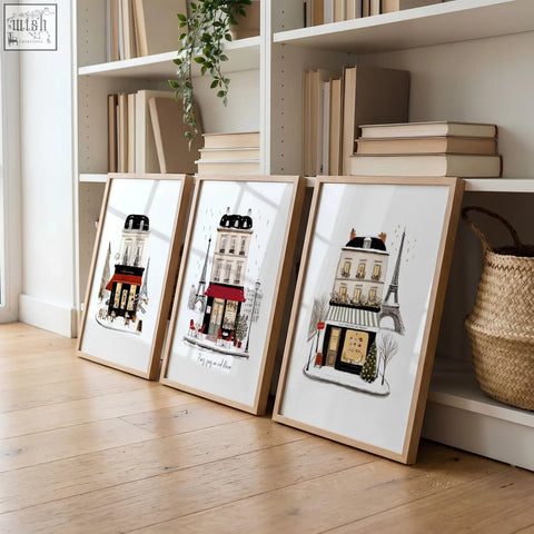 Three framed parisian street scene prints in black red and beige leaning against a white bookshelf perfect for living room wall art