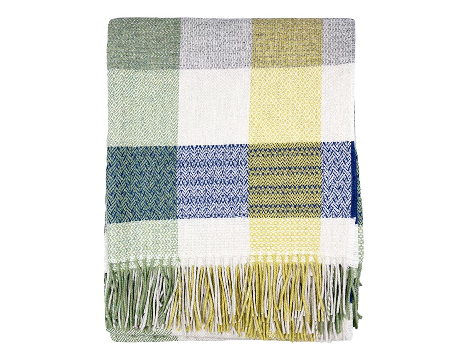 A soft patchwork merino lambswool throw in muted greens creams blues and yellows with herringbone texture