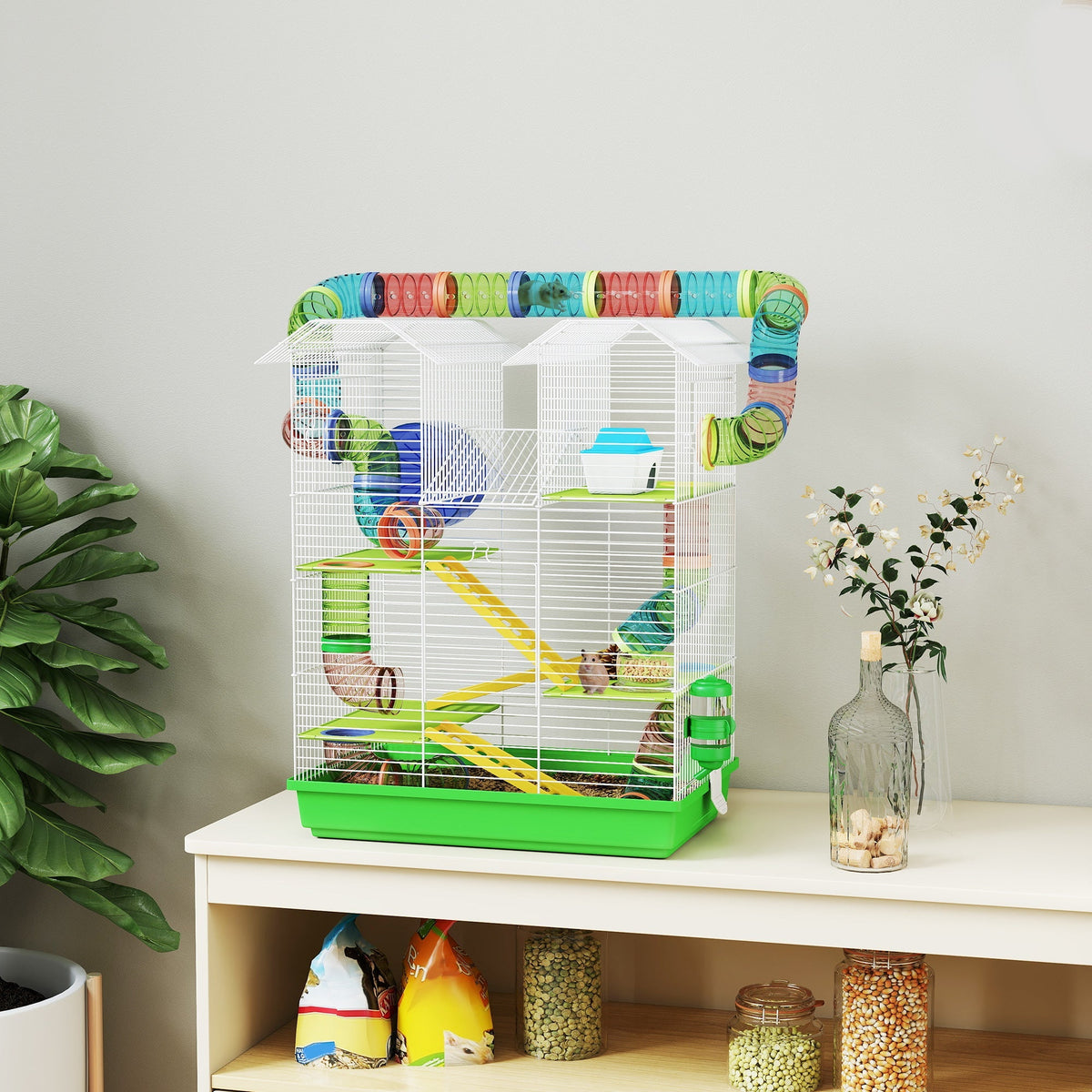 Colorful plastic tunnel atop a white wire hamster cage with green base yellow ramps and exercise wheels and water bottle