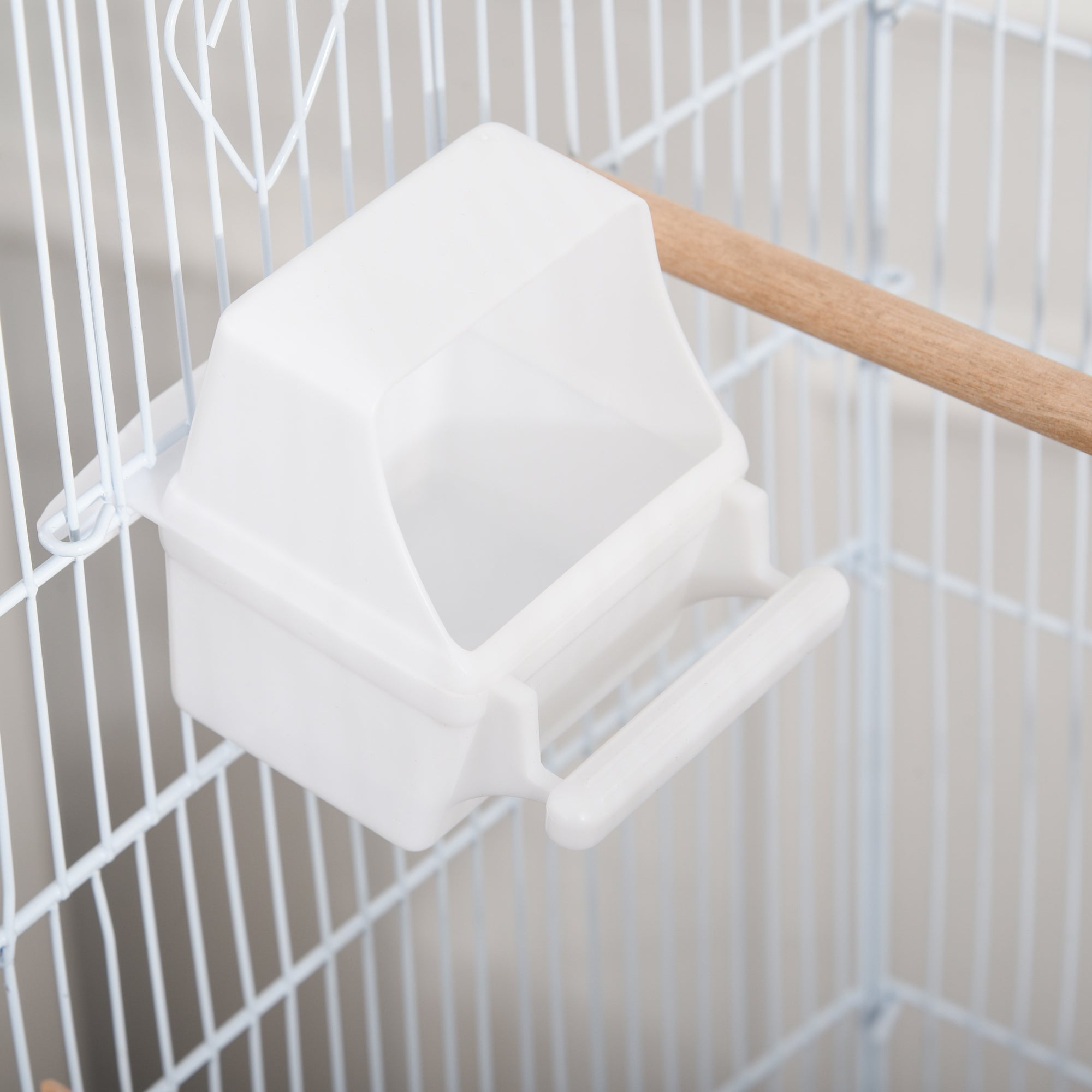 White plastic bird feeder with handle and hook hanging inside pawhut powder-coated metal bird cage with four wheels