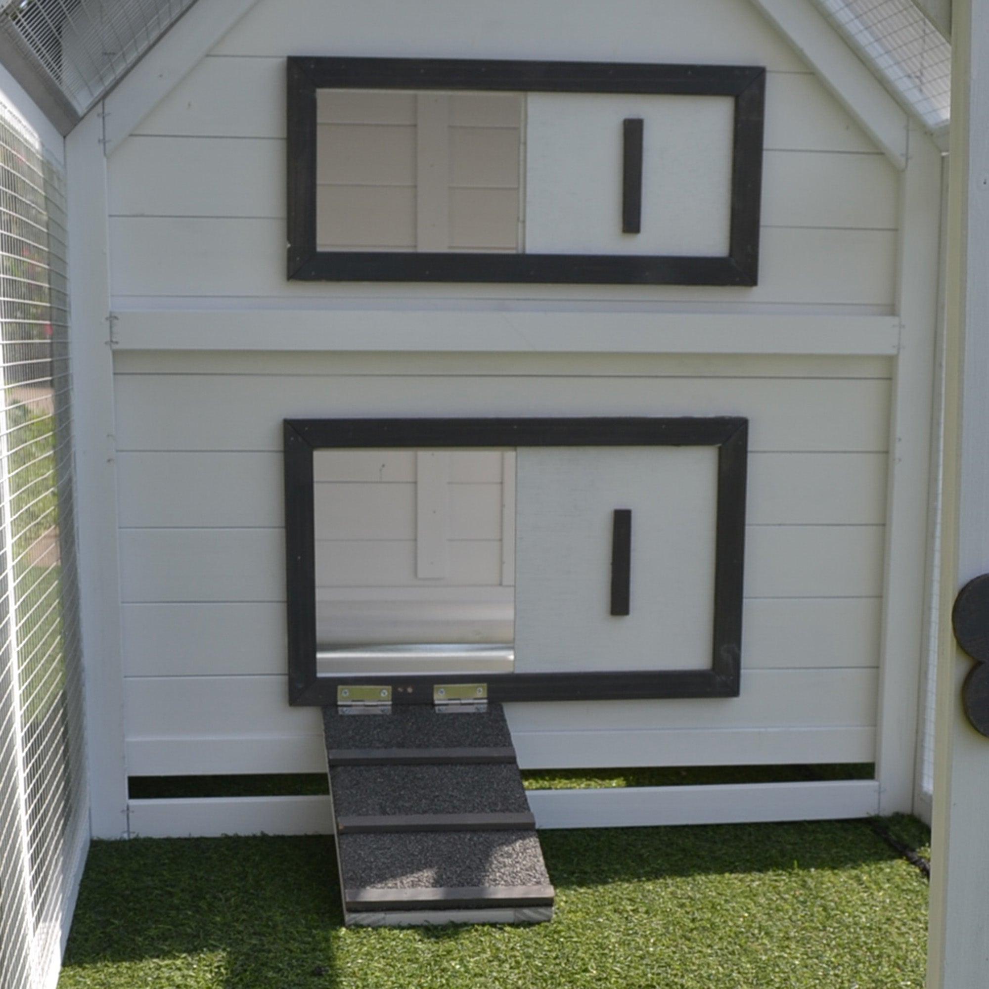 White fir wood chicken coop with black-framed windows sliding door and nesting box with small ramp entrance