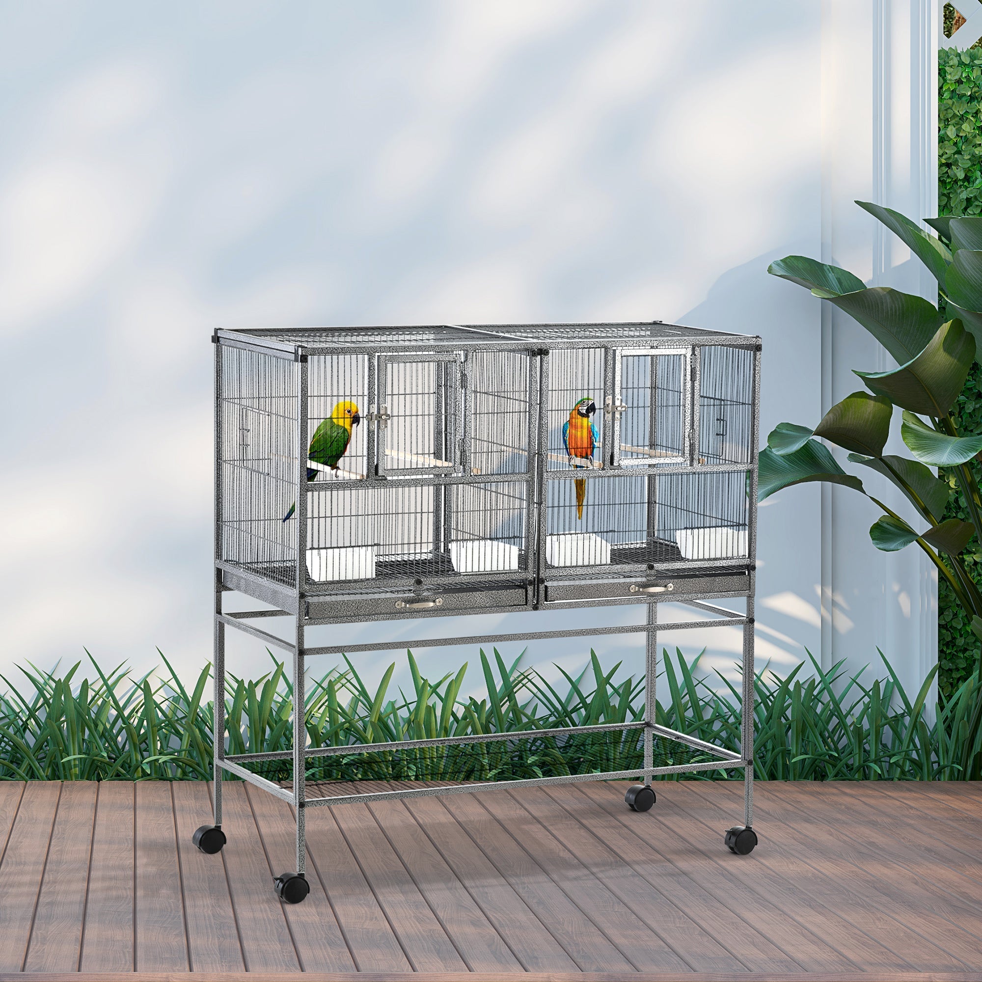 Silver metal bird cage with divider and slide-out metal trays housing colorful parrots with plastic food containers