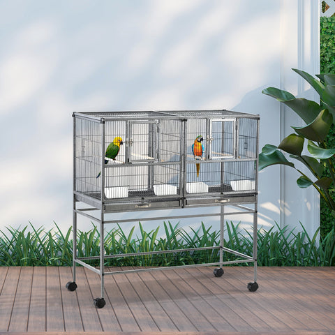 Silver metal bird cage with divider and slide-out metal trays housing colorful parrots with plastic food containers