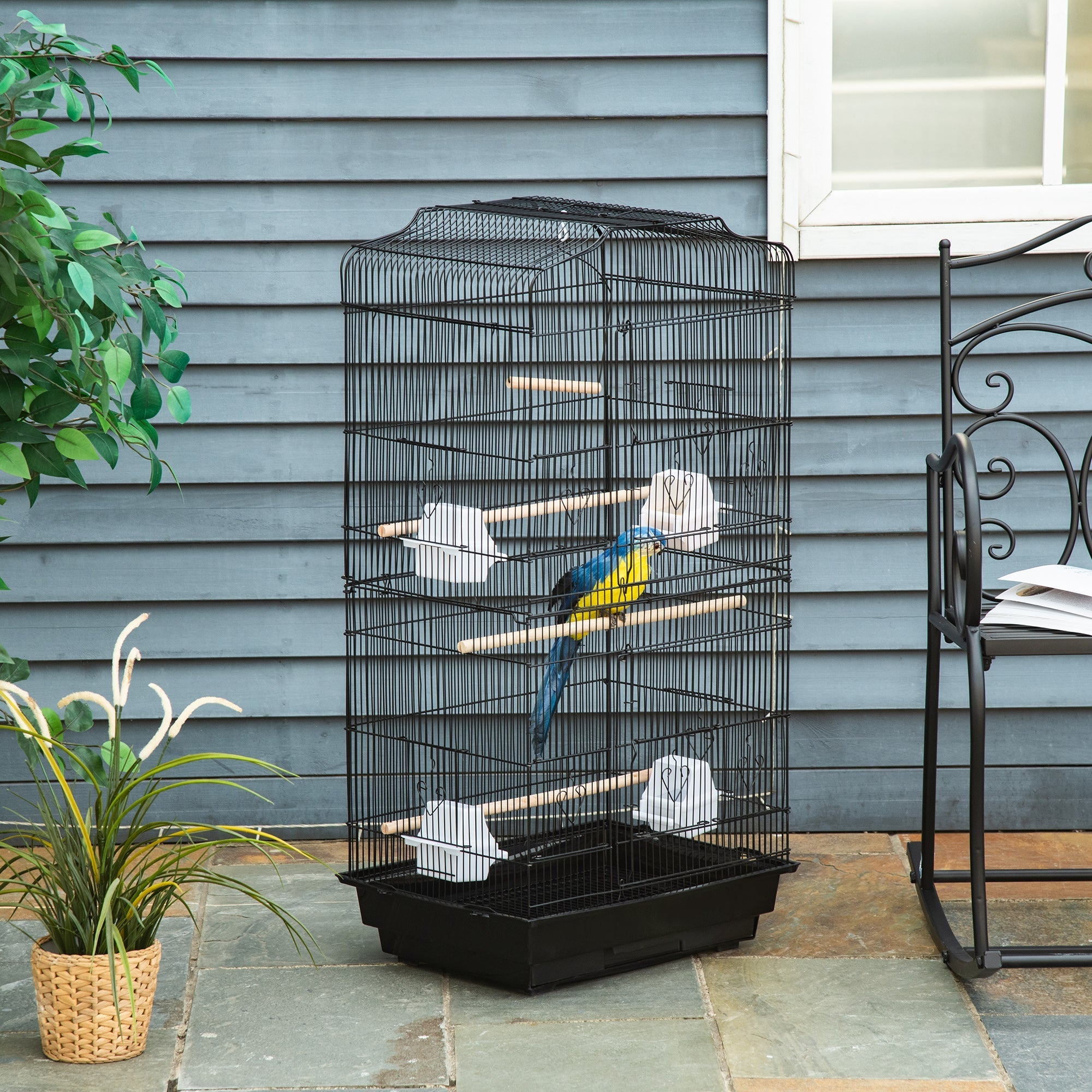 Black metal bird cage with wooden perches, two large food bowls, and a blue yellow parrot inside by PawHut