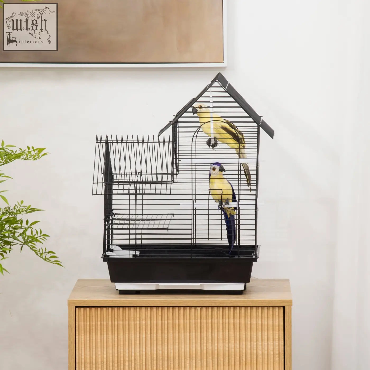 Black metal bird cage with house-shaped roof, two yellow parrots inside, swing ring and food containers included