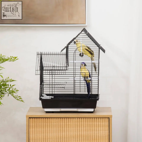 Black metal bird cage with house-shaped roof, two yellow parrots inside, swing ring and food containers included