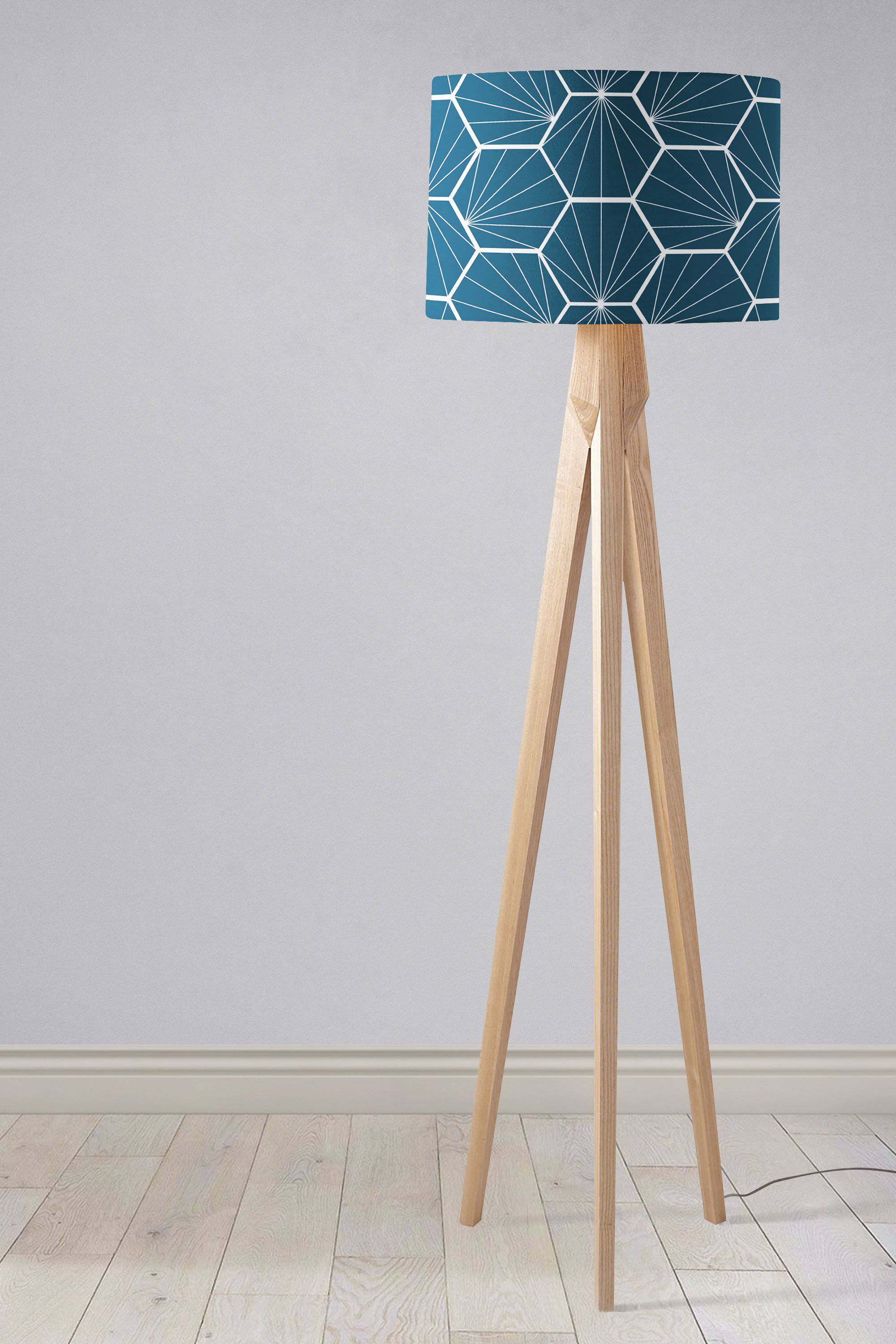 A modern tripod table lamp with a peacock blue fabric shade featuring a white hexagon design and light wood legs