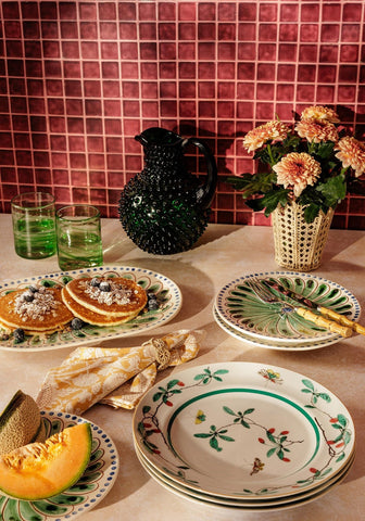 Stack of white ceramic peacock side plates with green and red botanical designs perfect for serving snacks