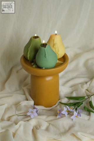 Three pear shaped candles in green and yellow on a mustard yellow ceramic pedestal perfect for cozy decor