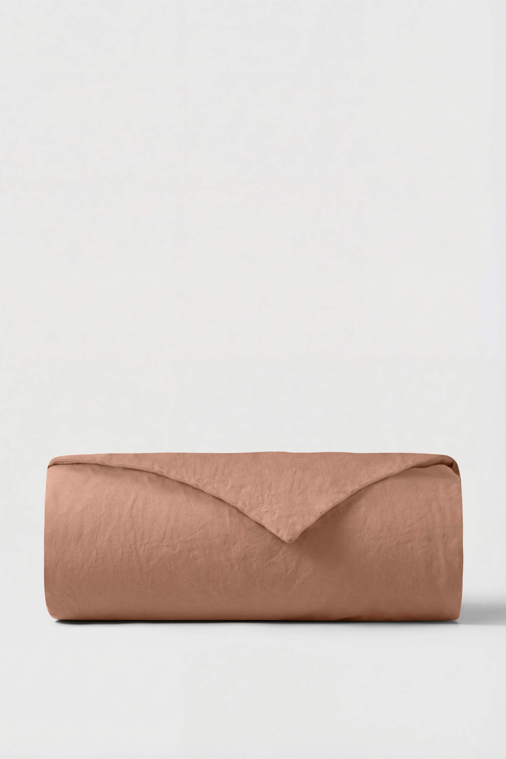 A neatly rolled terracotta percale duvet cover made of soft linen with a textured surface and clean fold
