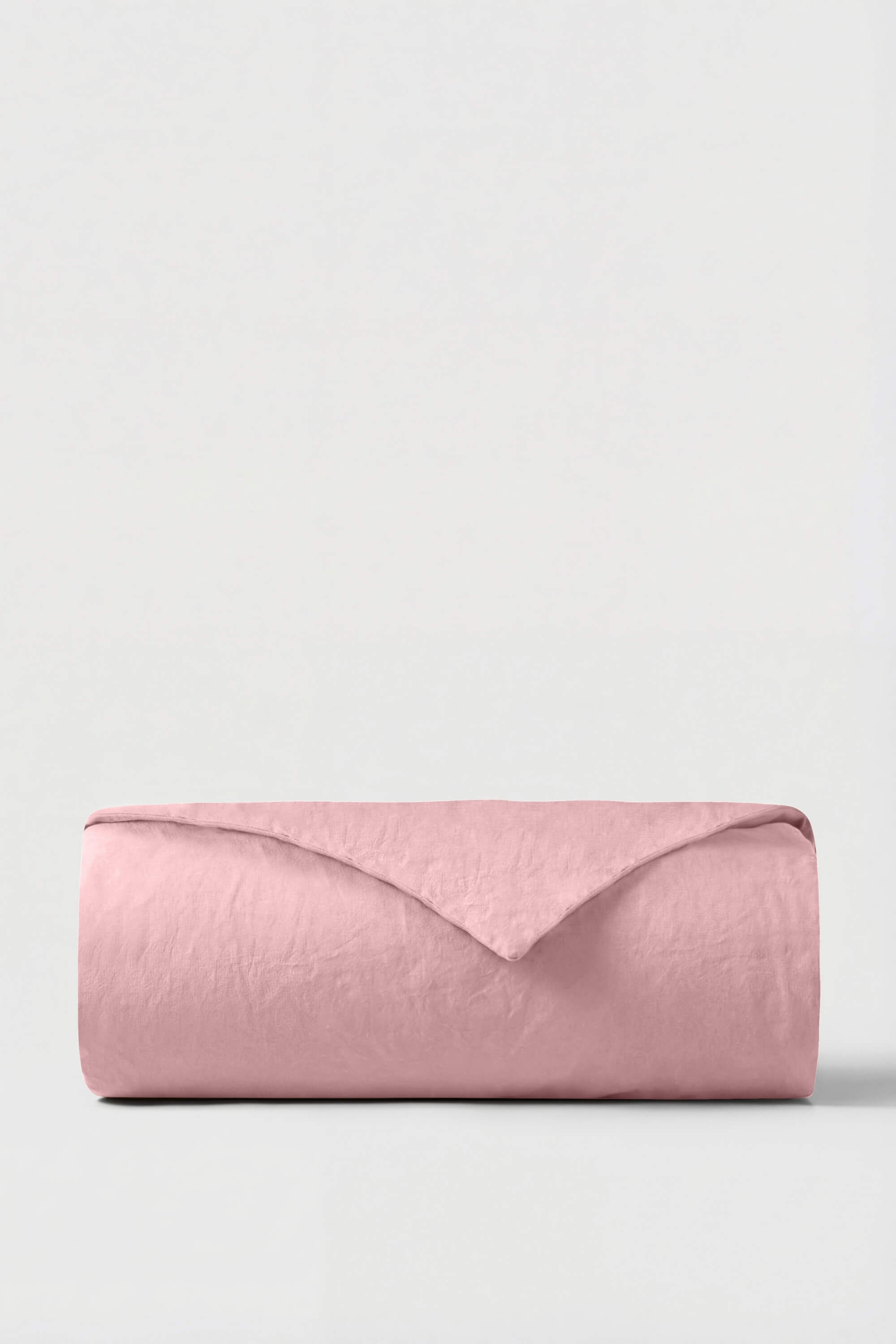 A soft pink linen percale duvet cover neatly rolled against a neutral background perfect for cozy bedding