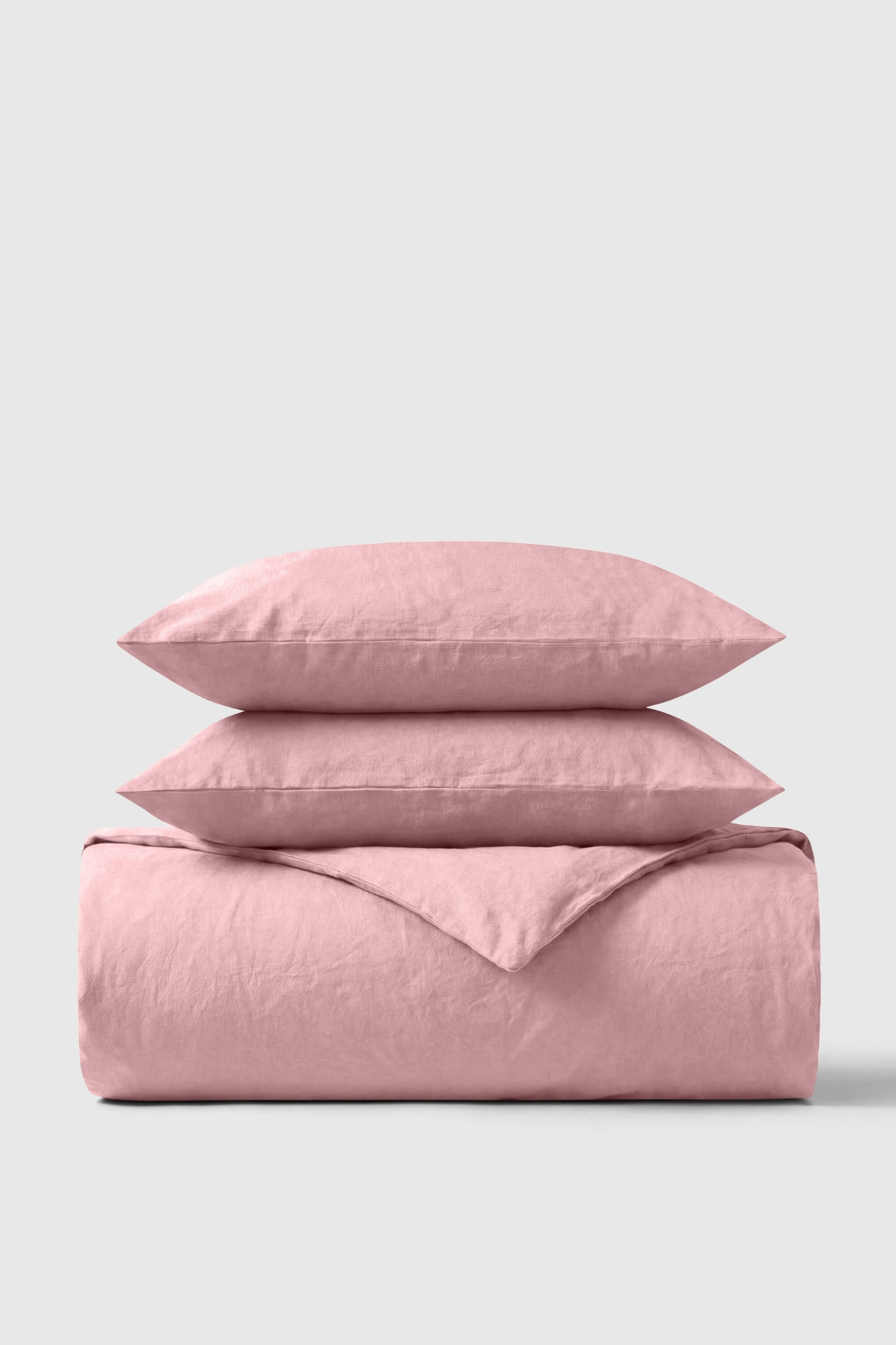 A soft pink percale duvet cover set with matching pillows neatly folded made from breathable linen fabric