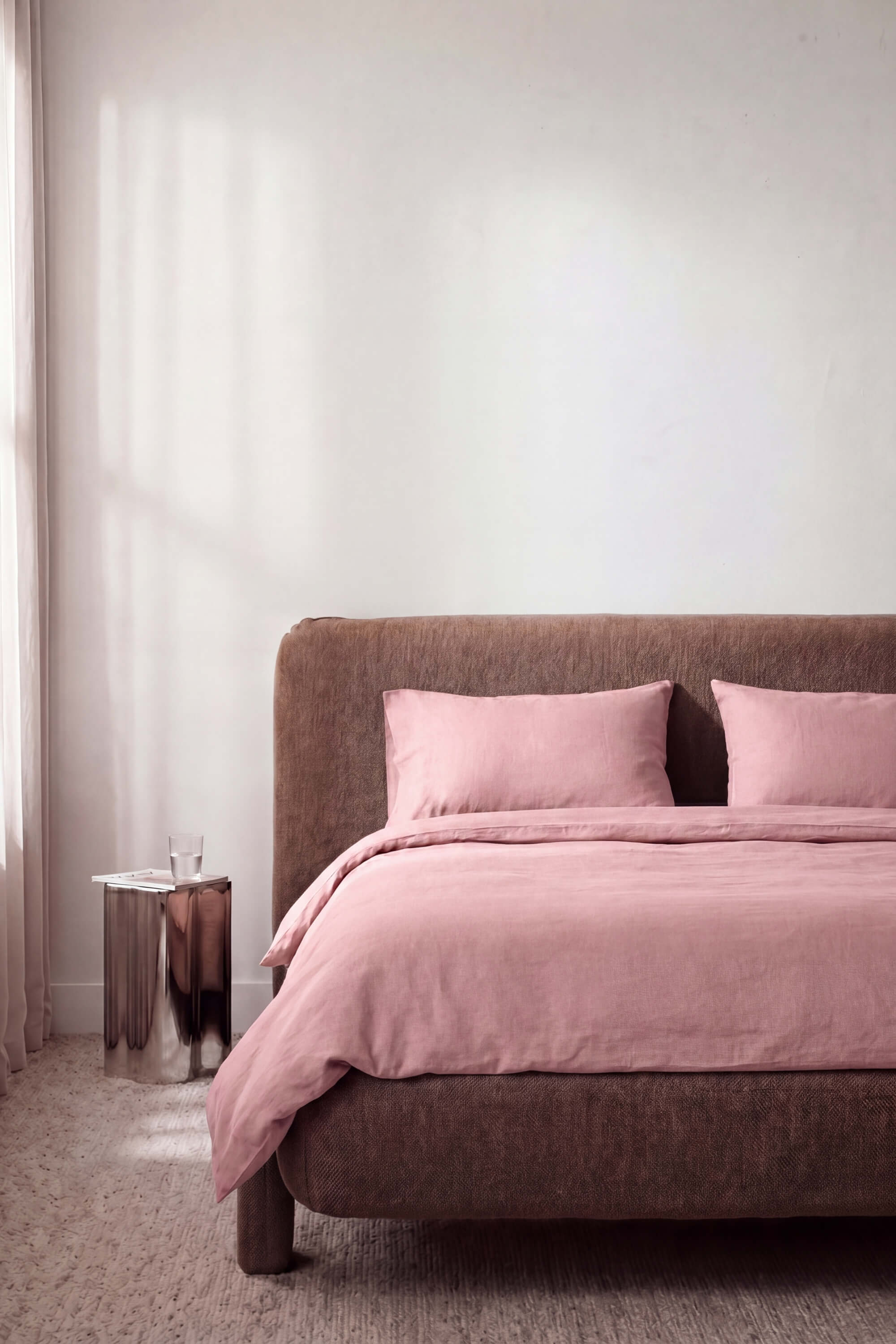 A plush dusty rose percale essentials bedding set with linen duvet and matching pillows on a textured brown bed frame