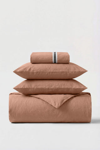 A soft terracotta cotton percale essentials bedding set with subtle textured weave and striped pillowcase band