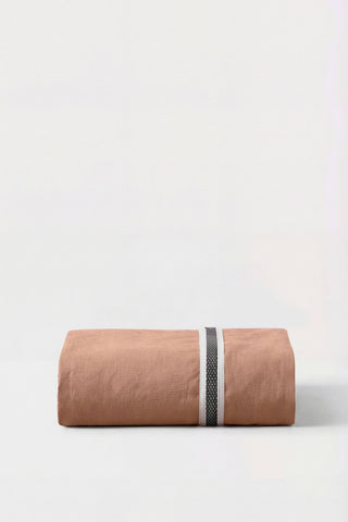 A terracotta linen percale fitted sheet neatly rolled with a black and white woven stripe detail in the center