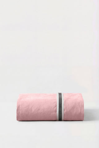 A soft pink linen duvet cover neatly rolled with a black and white band shown with percale fitted sheet