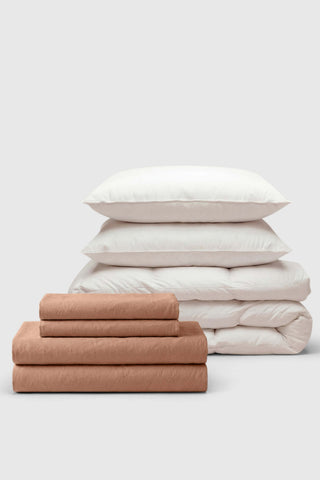 A neatly stacked percale move-in bedding set with soft terracotta and off-white pillows featuring a subtle weave