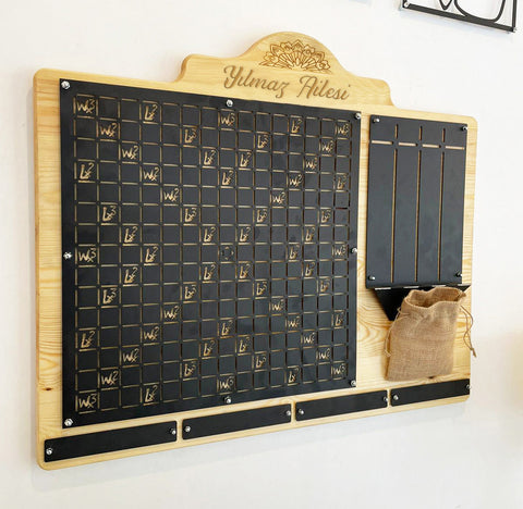 Light wood framed family calendar board with black panels gold engraved text decorative motifs for words wall deco