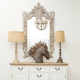 Silver ornate mirror with intricate detailing reflecting a decorative chandelier near the petra table lamp