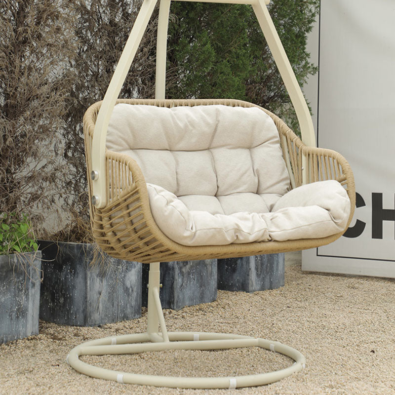 Beige woven rattan garden hanging egg chair with cream cushions and curved metal stand for indoor outdoor use