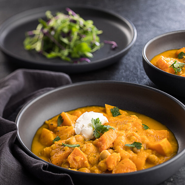 A rich orange sweet potato curry served in a matte black pico black coupe plate 7 inch bowl with yogurt garnish