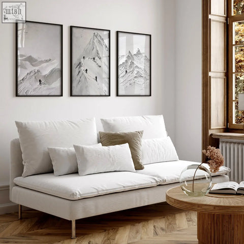 White upholstered sofa with metallic legs and cushions below scandi mountain climbers wall art prints on living room walls
