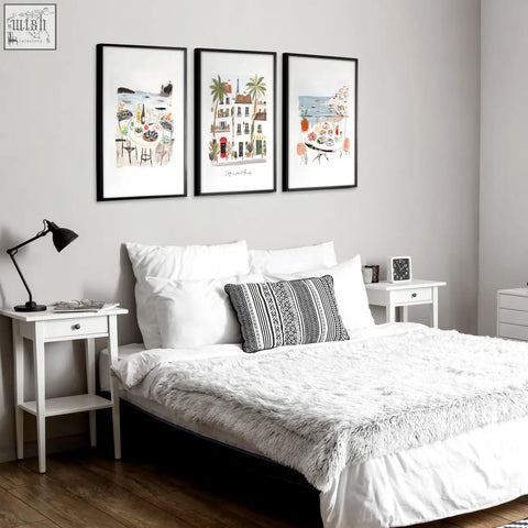 Black-framed sotto il sole wall art prints featuring european seaside towns hang above the bed in bedroom coastal decor
