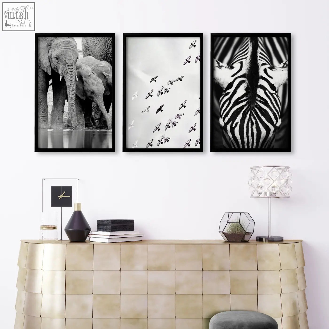 Three black-framed black and white wildlife art prints of elephants birds and zebra mounted on a living room wall above gold console