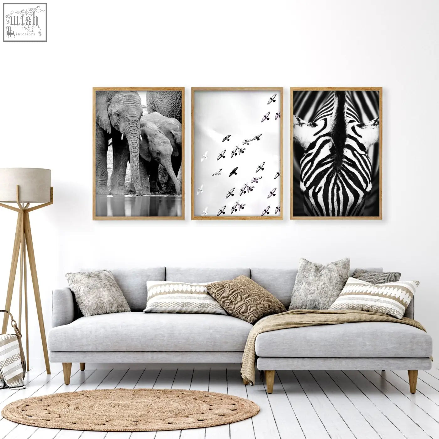 Three framed black and white wildlife safari art prints of elephants birds and zebra hang on a living room wall above a gray sofa