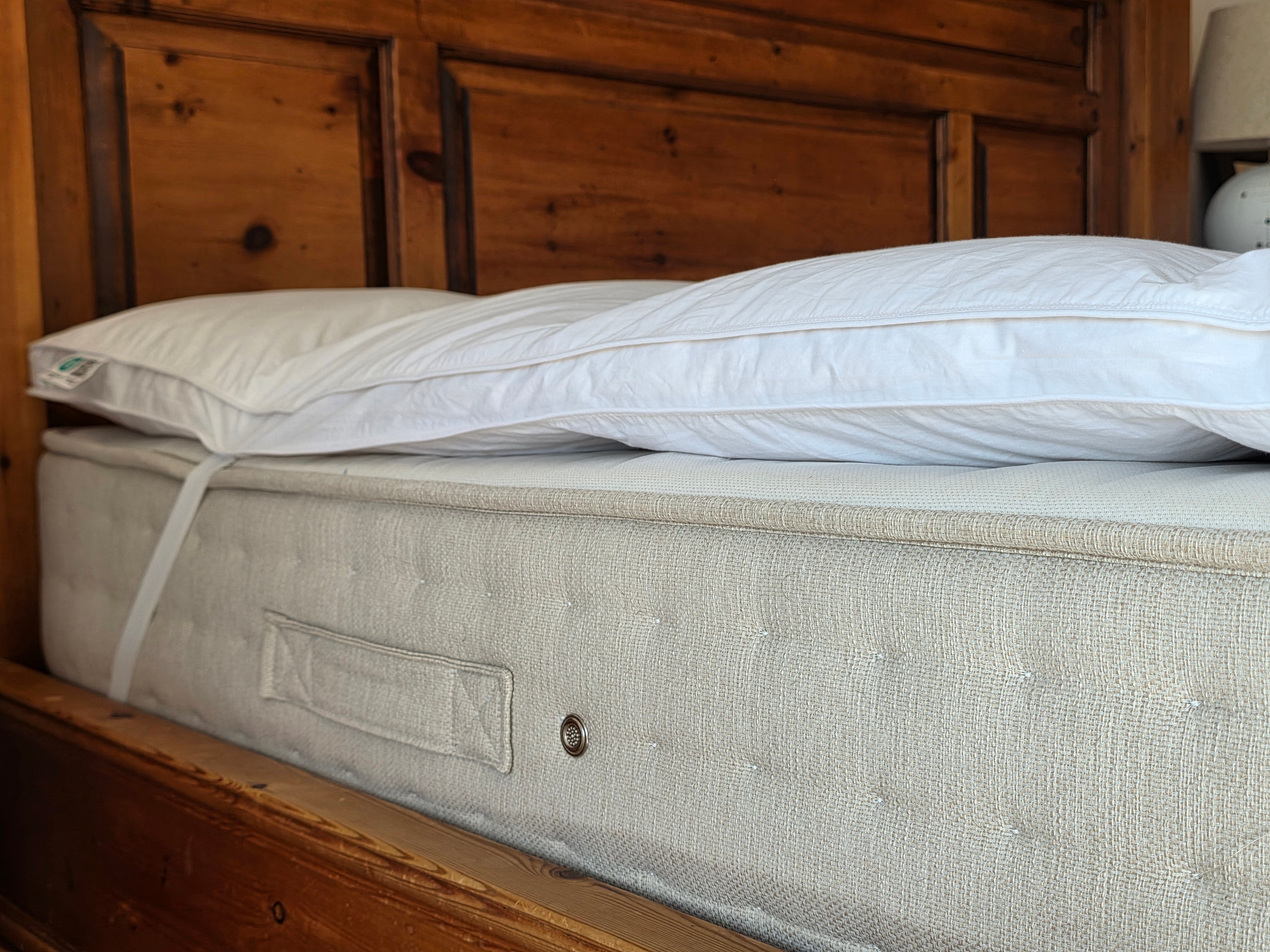 Light gray tufted mattress topper with white pillow featuring duck feather filling for comfy sleep solutions