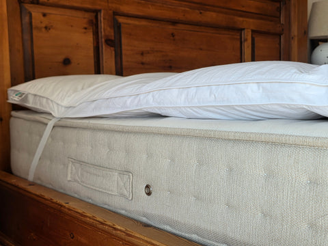 Light gray tufted mattress topper with white pillow featuring duck feather filling for comfy sleep solutions