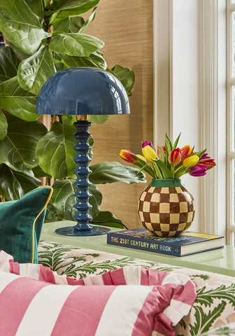 A glossy navy blue dome-shaped table lamp with a twisted ribbed base next to a pink candy cabana stripe ruffled cushion cover