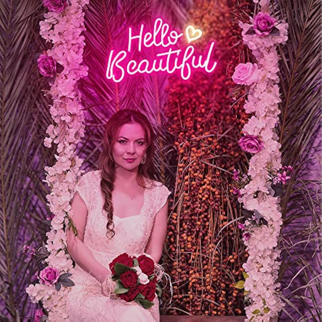 A woman in a white lace wedding gown holds red roses next to a pink hello beautiful neon sign with white heart ambient glow night light