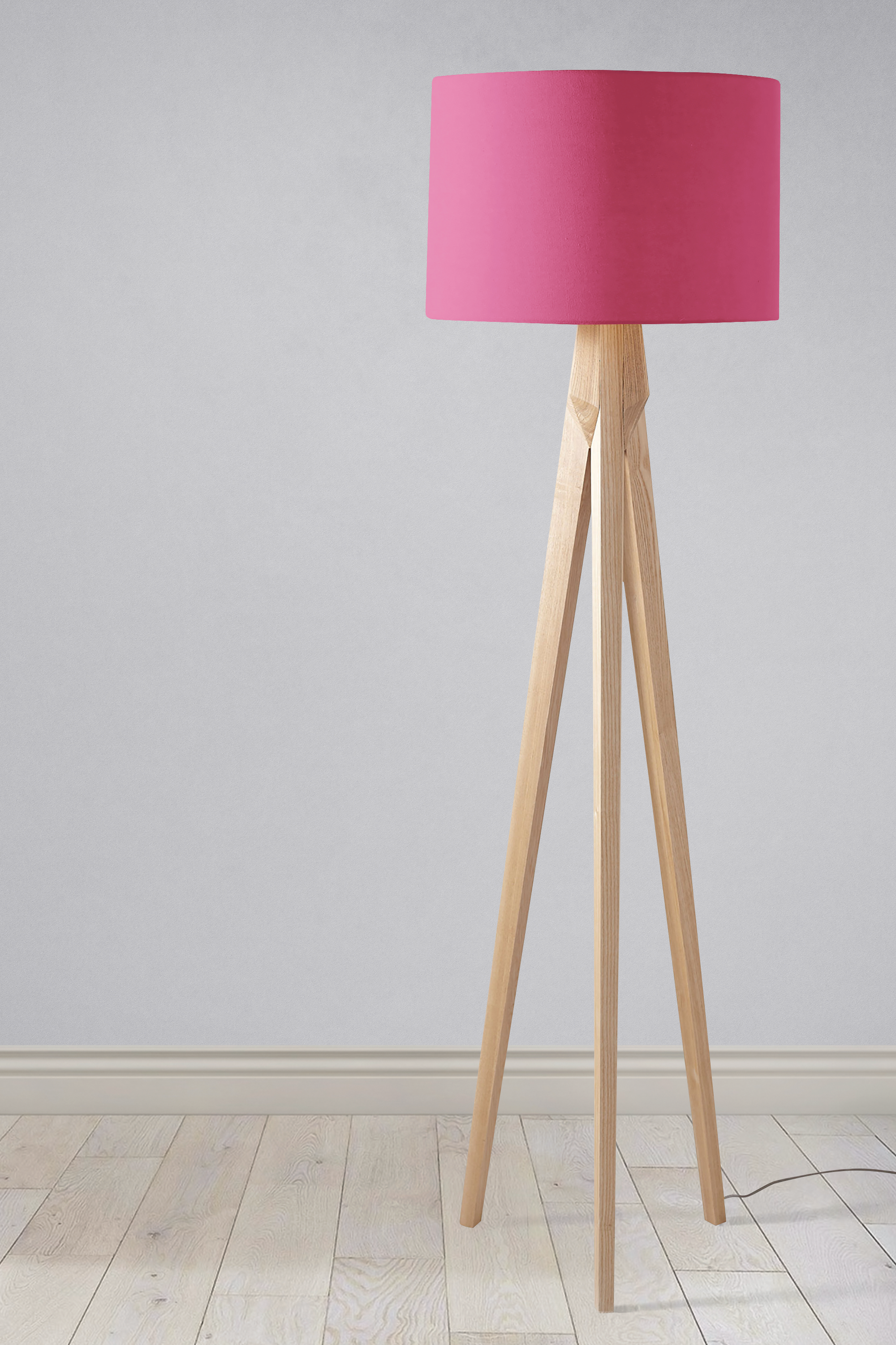 A modern tripod floor lamp with a plain cerise pink lampshade and light wooden legs perfect as a table lamp