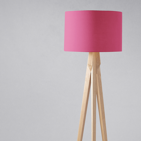 A plain cerise pink lampshade with a vibrant pink cylindrical shade on a light wooden tripod table lamp base