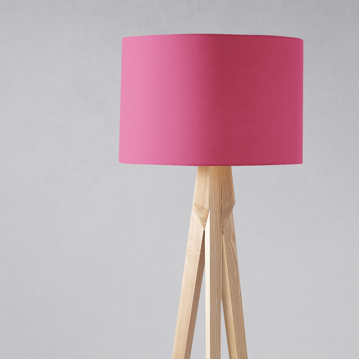 Plain cerise pink lampshade with vibrant pink cylindrical shade on a light wooden tripod table lamp base