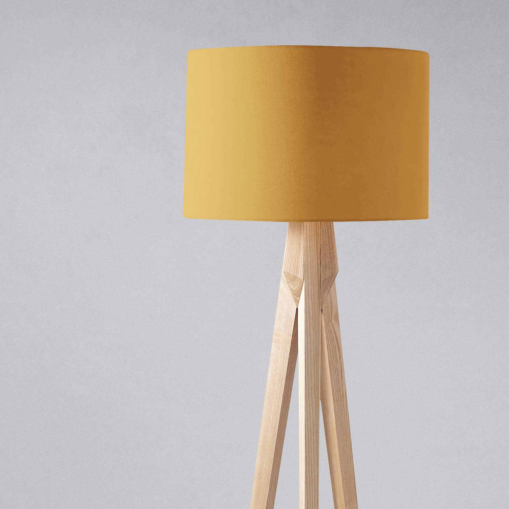 A plain mustard cylindrical lampshade on a light wooden tripod base for table lamp use