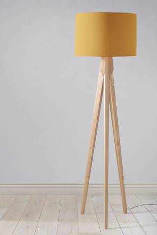 A modern tripod floor lamp with a plain mustard lampshade and light wooden legs perfect as a table lamp