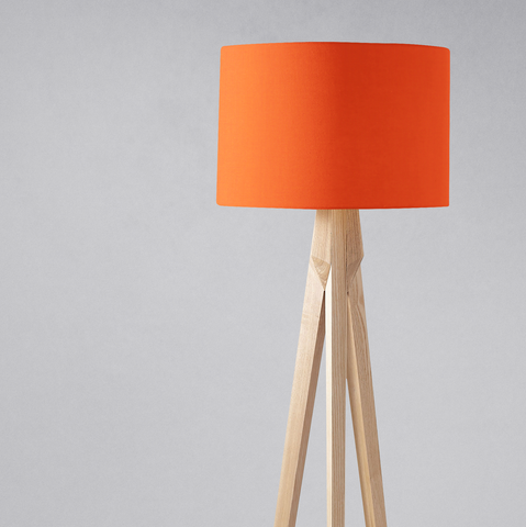Orange lampshade with a plain cylindrical design mounted on a light wood tripod table lamp base