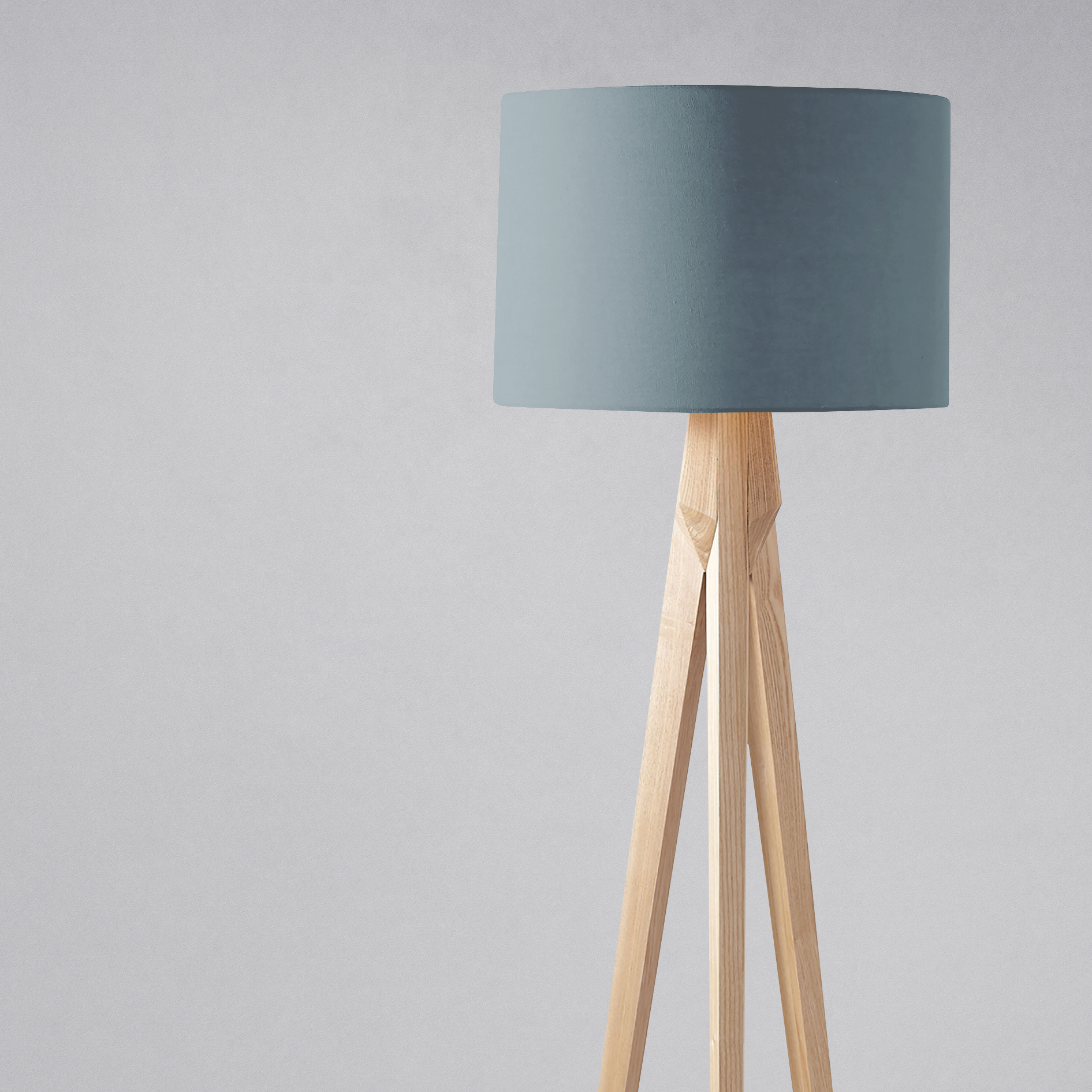 A minimalist tripod floor lamp with a plain petrol blue fabric lampshade and light wooden legs perfect for a table lamp setup