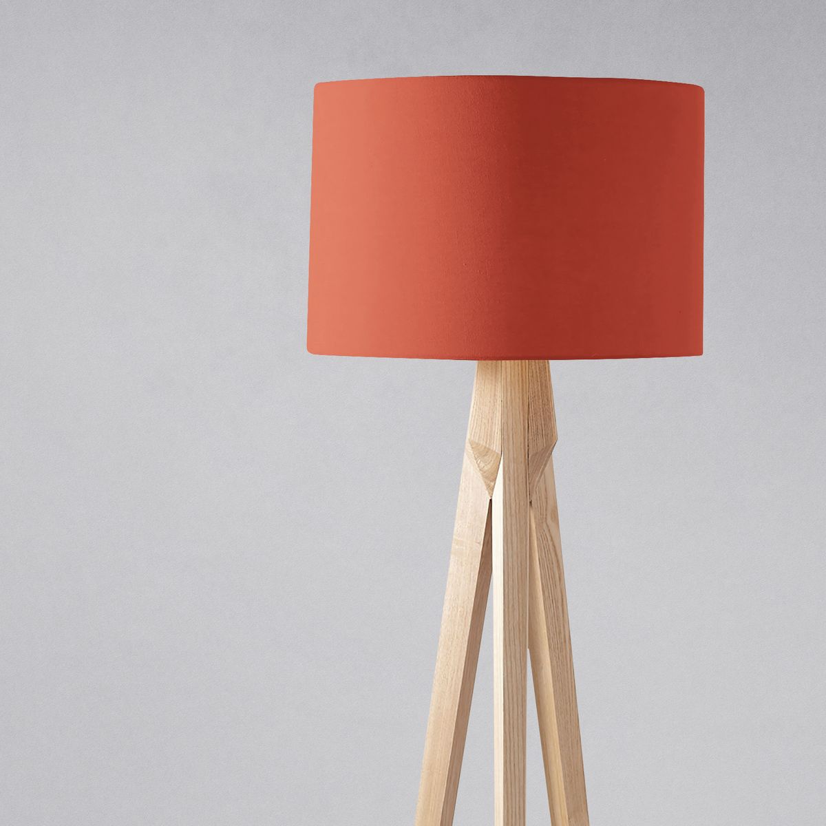 A modern table lamp with a plain rust lampshade in matte coral fabric and light wooden tripod legs