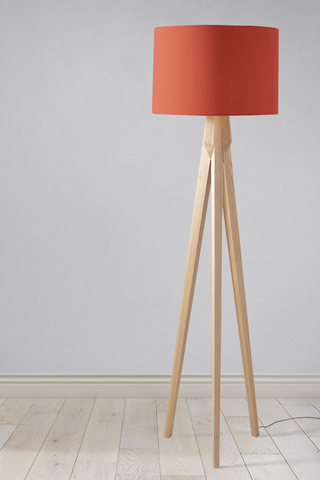 A modern table lamp with a plain rust lampshade in vibrant coral fabric and light wooden tripod legs
