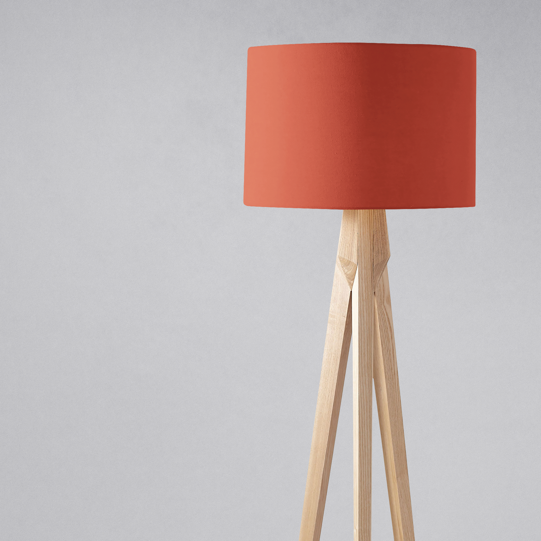 A plain rust lampshade made of terracotta fabric on a light wood tripod base perfect for a table lamp