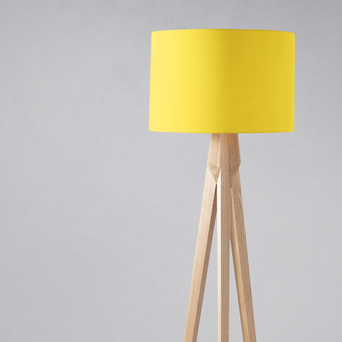 A plain yellow lampshade made of fabric on a light wooden tripod base perfect for a table lamp