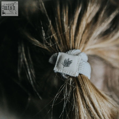 A soft light gray plastic free hair tie with woven texture and embroidered leaf, part of a 6 pack black set organic cotton