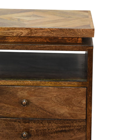 A rustic wooden platform bedside table with a herringbone top and two drawers with brass knobs