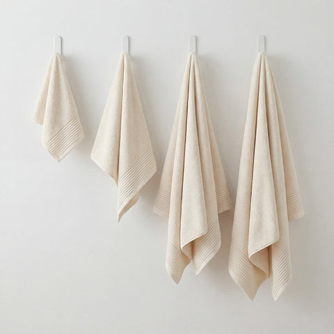 Set of four cream-colored plush towels made of cotton with ribbed hems hanging neatly on white hooks