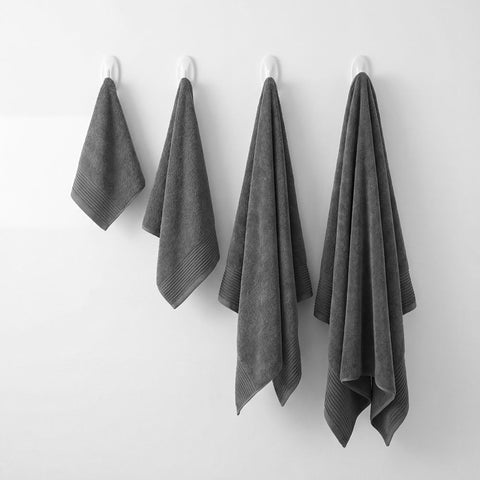 Four dark gray plush towels set with ribbed hems hanging neatly from white hooks for bathroom use