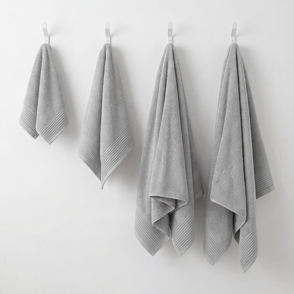 Four light gray plush towels set with ribbed hemmed edges hanging neatly on white hooks